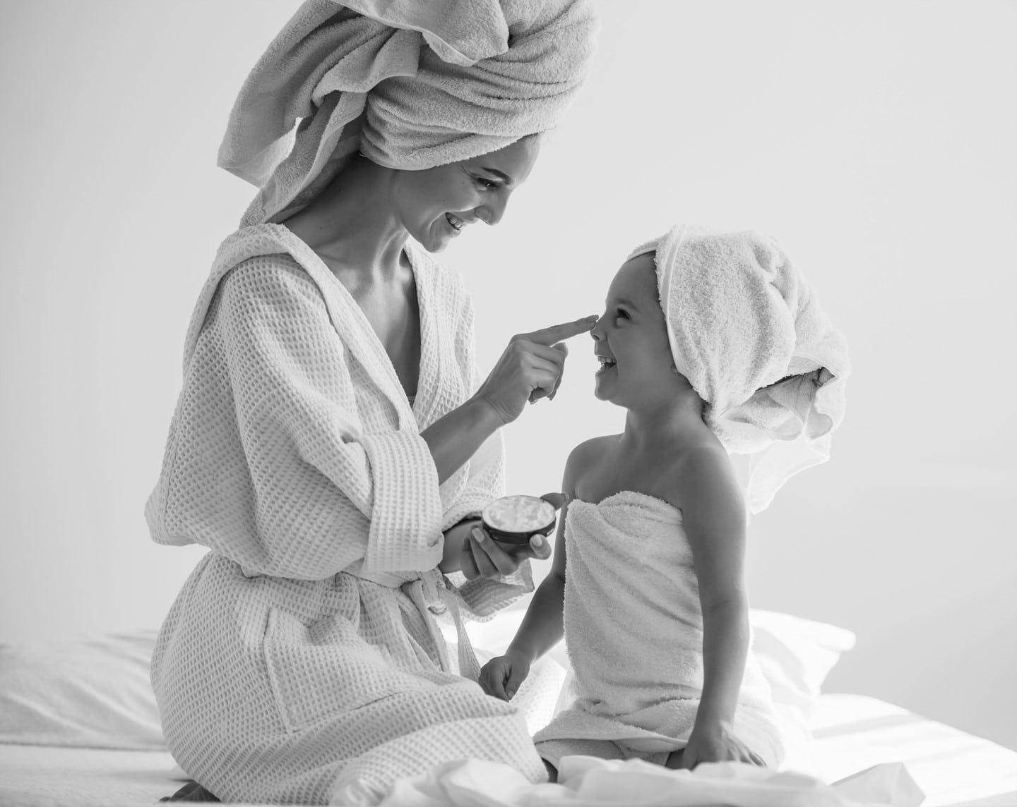 Smiling mother in a bathrobe with towel wrapped hair playing with smiling child wrapped in towel