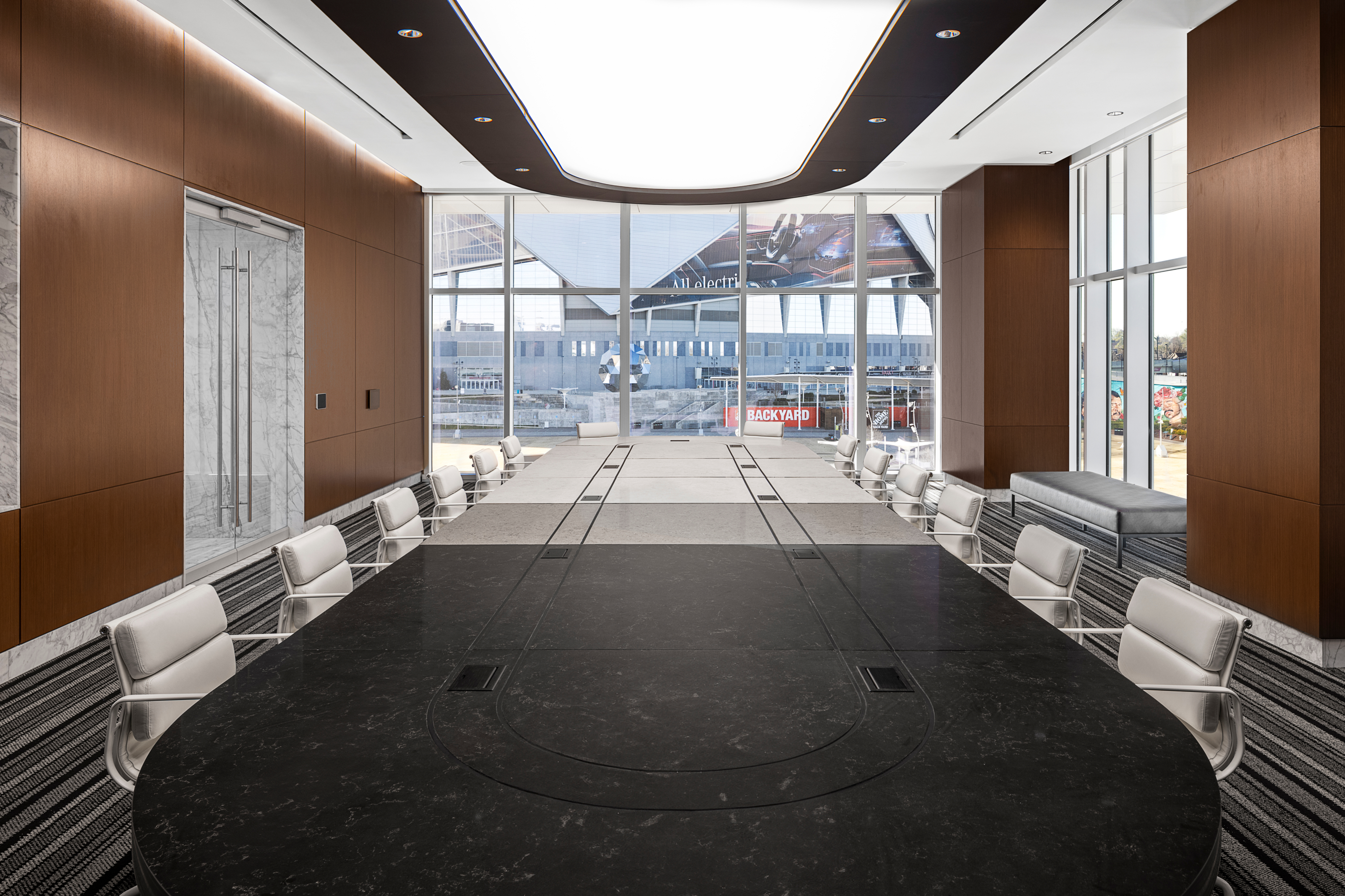 Sleek boardroom featuring a long oval black table, encircled by white chairs. Large windows let in natural light and offer a lightning-quick glimpse of the bustling industrial construction site beyond.