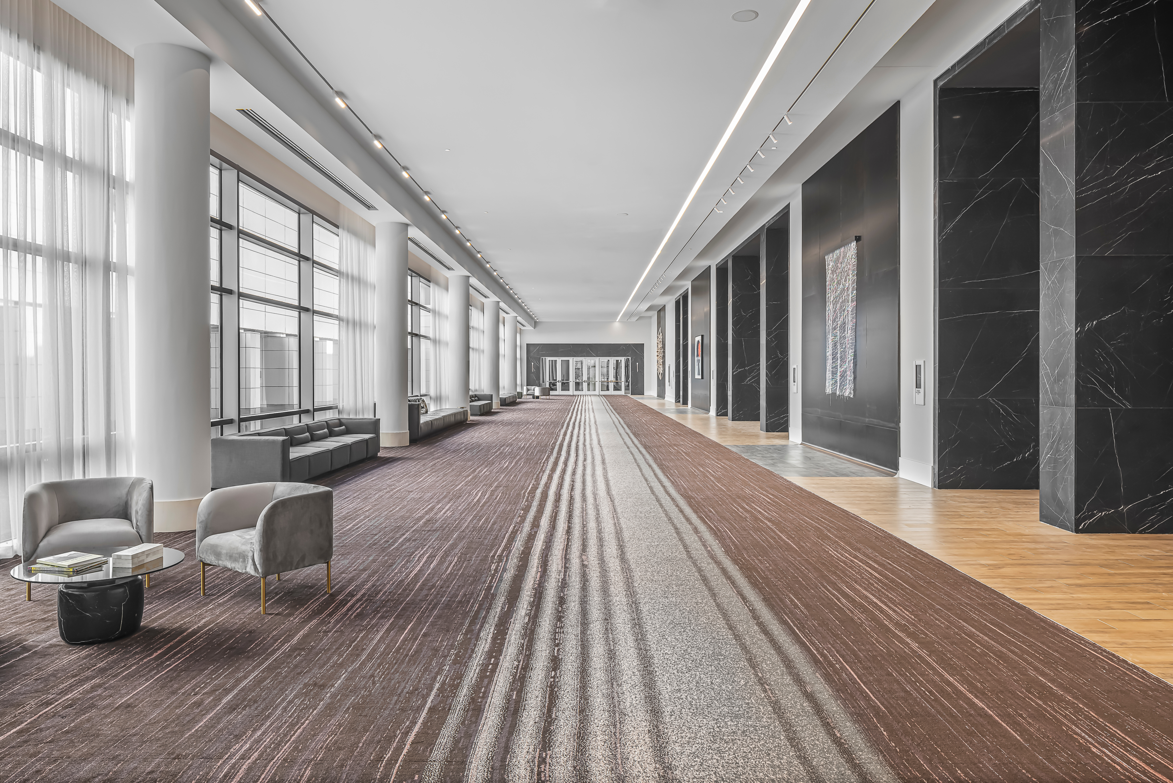 Spacious modern hallway with large windows and high ceilings, reminiscent of a triumph ballroom, featuring seating areas with armchairs and tables. Decorative columns and artworks adorn the walls, making it an ideal event venue.