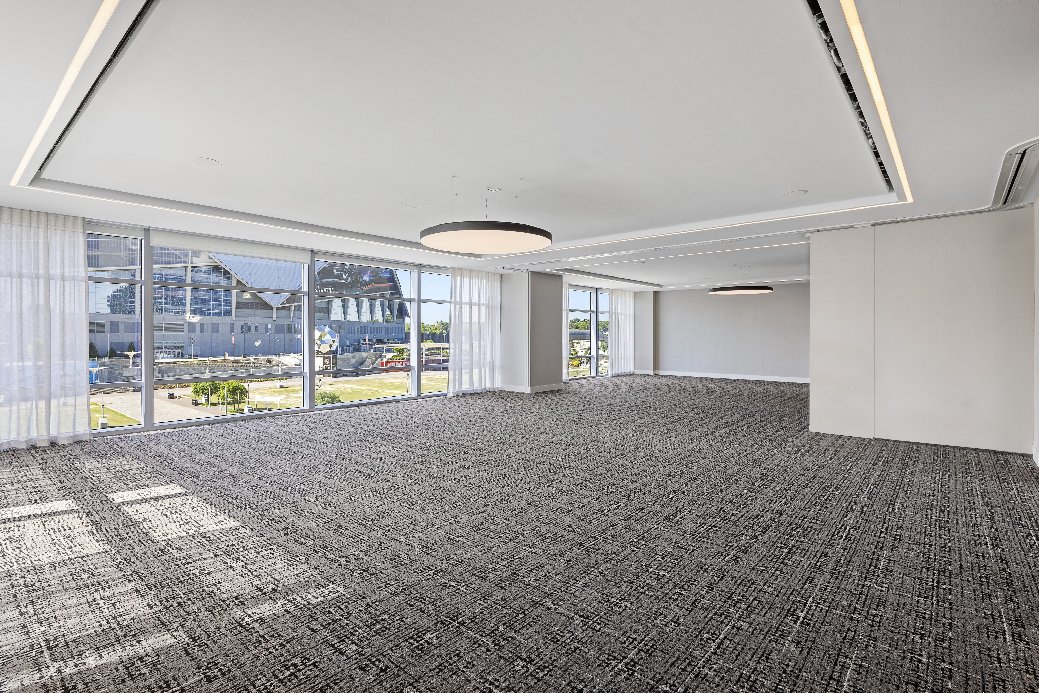 A spacious, empty meeting room with patterned carpet, large windows, and a circular ceiling light. Outside, a view of a magnificent modern building and the cityscape is visible.