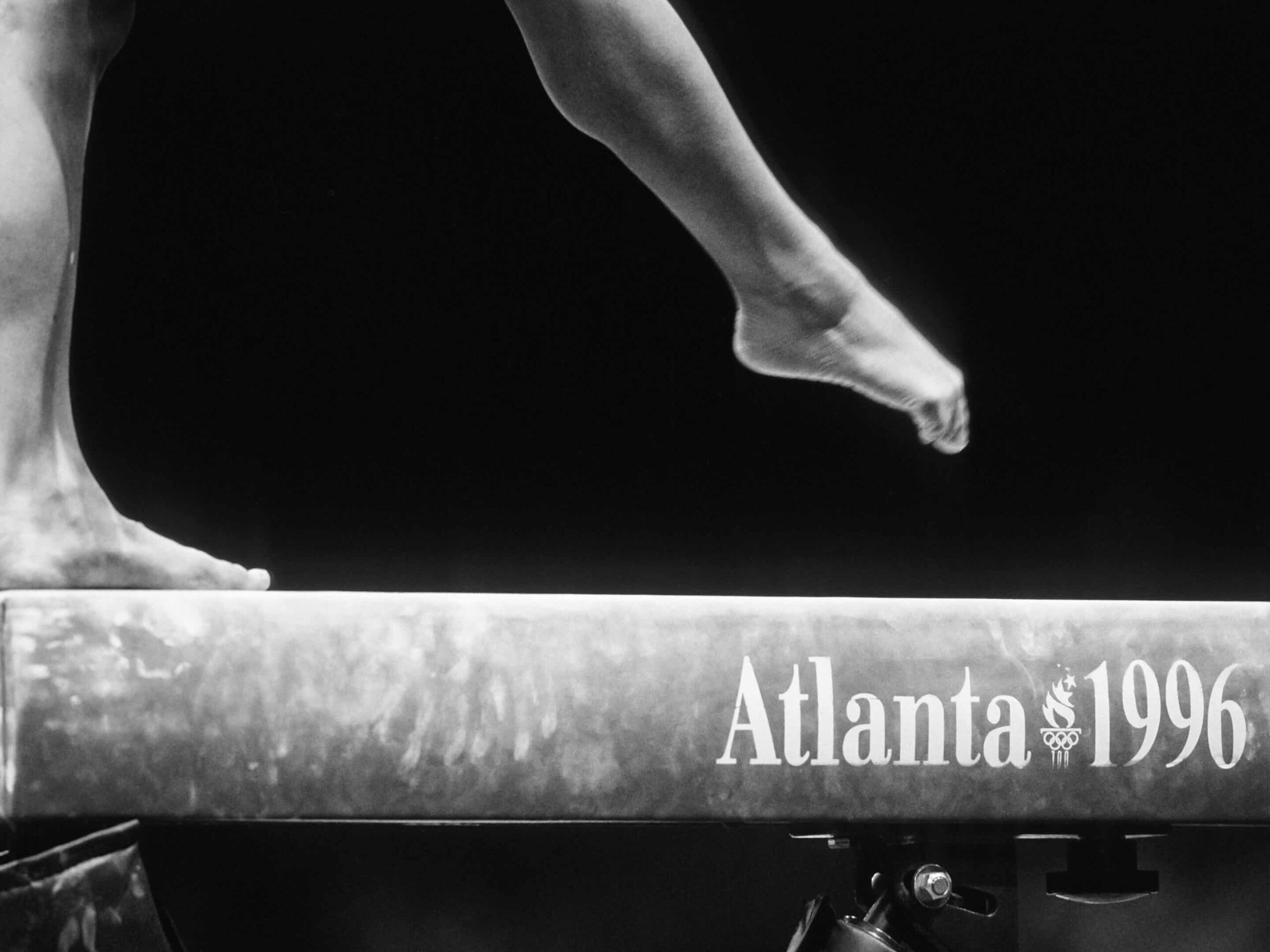 Close-up of a gymnast's feet on a balance beam with "Atlanta 1996" text, capturing the elegance of Olympic Games—a precision akin to navigating the focus required in Type I Meeting Rooms.