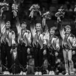 A gymnastics team stands on a podium in matching uniforms, holding flowers and medals, celebrating their achievement just like a team in Type II Meeting Rooms celebrates sealing a successful deal.