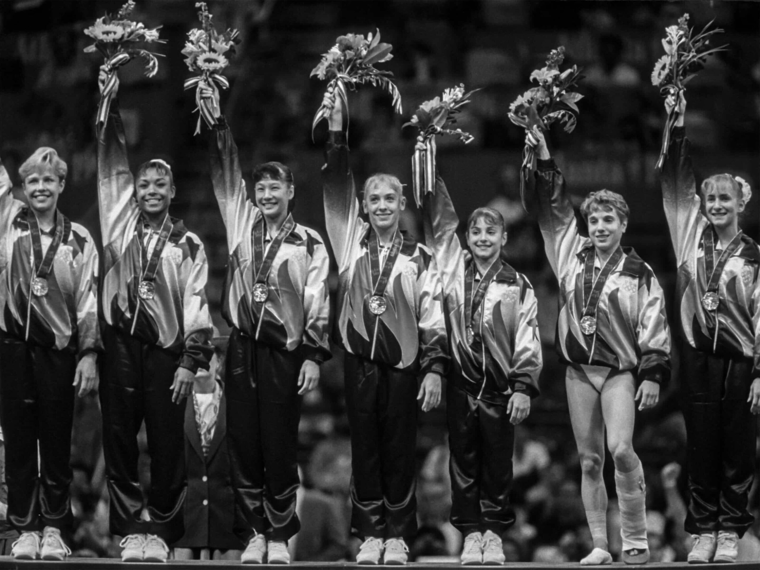 A gymnastics team stands on a podium in matching uniforms, holding flowers and medals, celebrating their achievement just like a team in Type II Meeting Rooms celebrates sealing a successful deal.