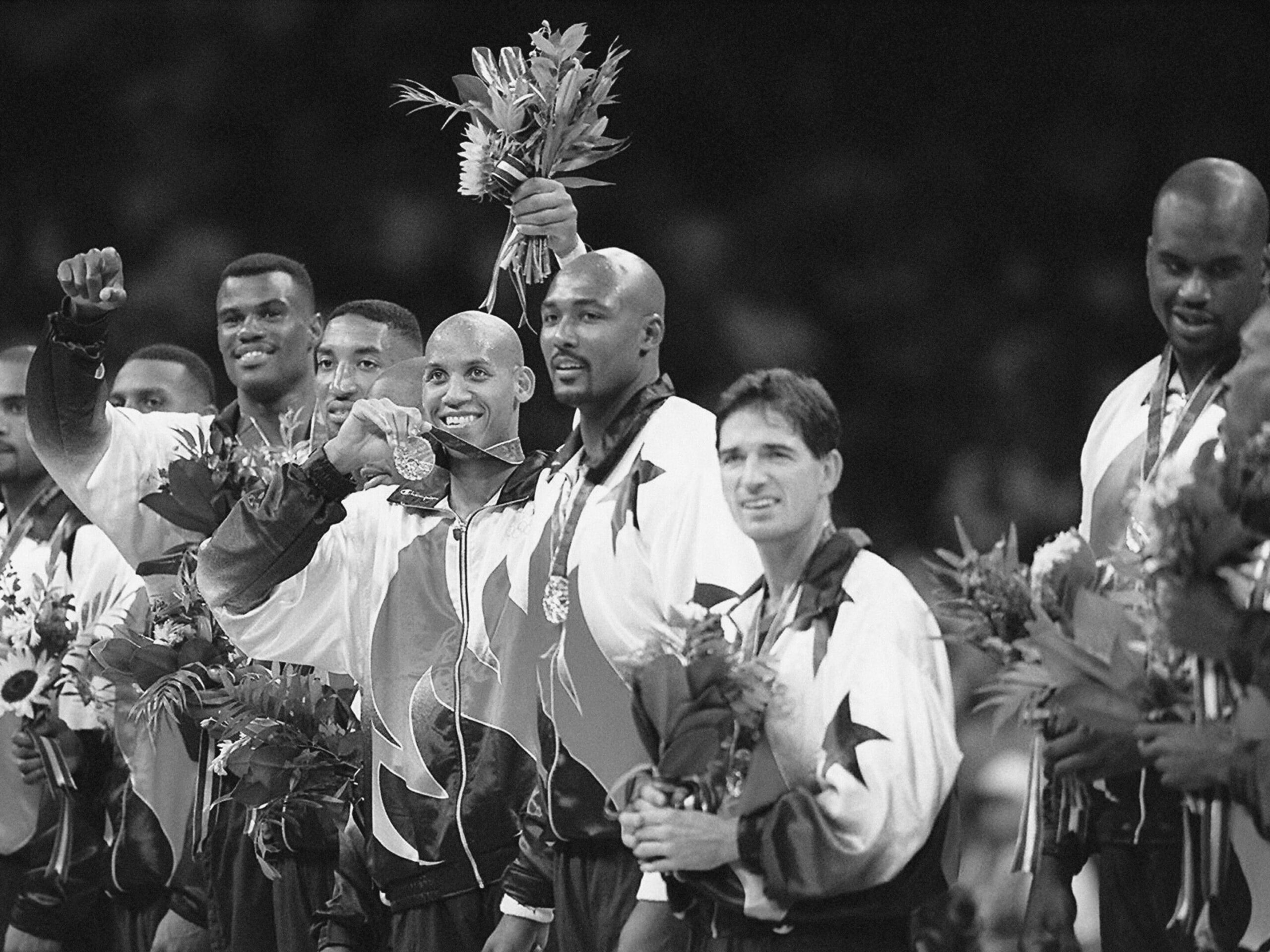 A basketball team poses together in a meeting room, proudly wearing matching uniforms and holding bouquets and medals.