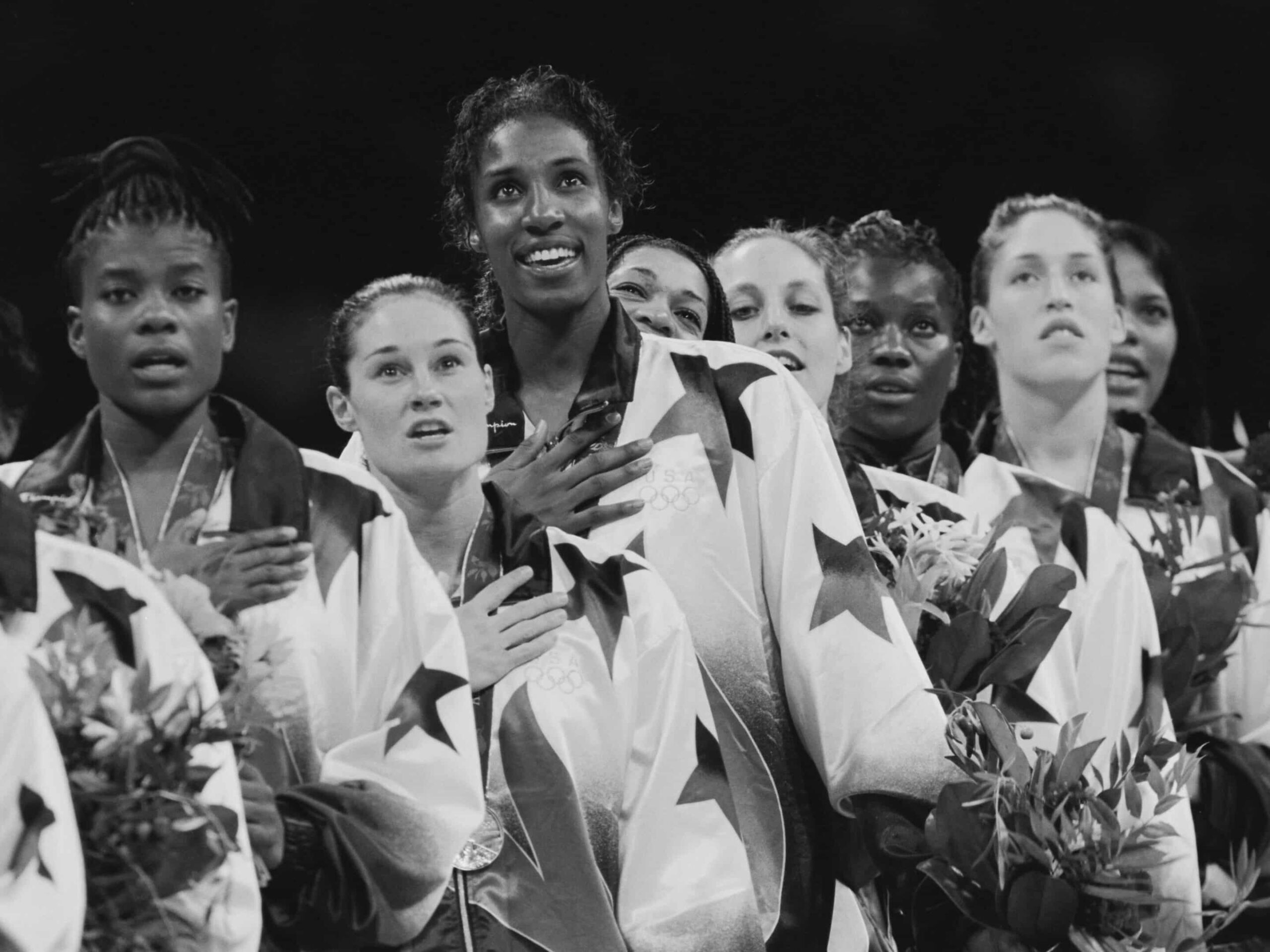 During a ceremony, a group of female athletes in star-patterned jackets stands with hands on hearts and holding bouquets. Their poised presence lends an atmosphere as formal as one might find in Type II Meeting Rooms.