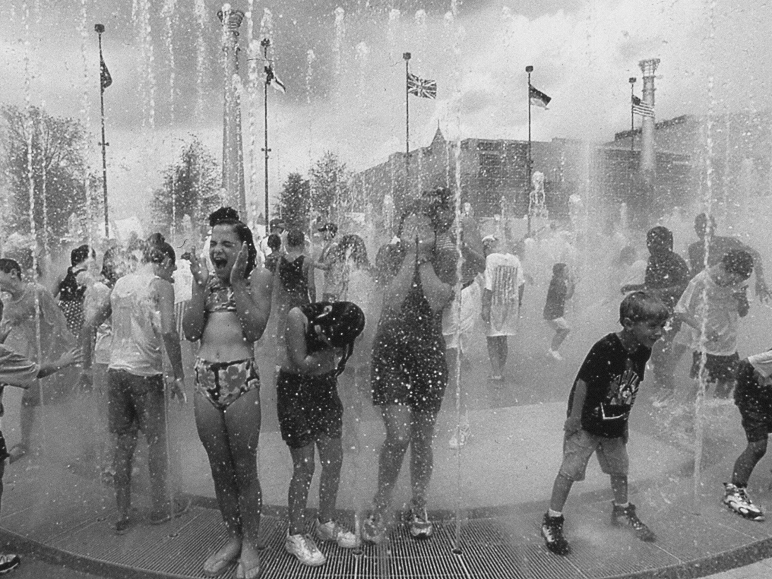 Children playing and laughing in an outdoor water fountain on a sunny day, their joy reminiscent of carefree moments captured in the GSU Digital Collections.