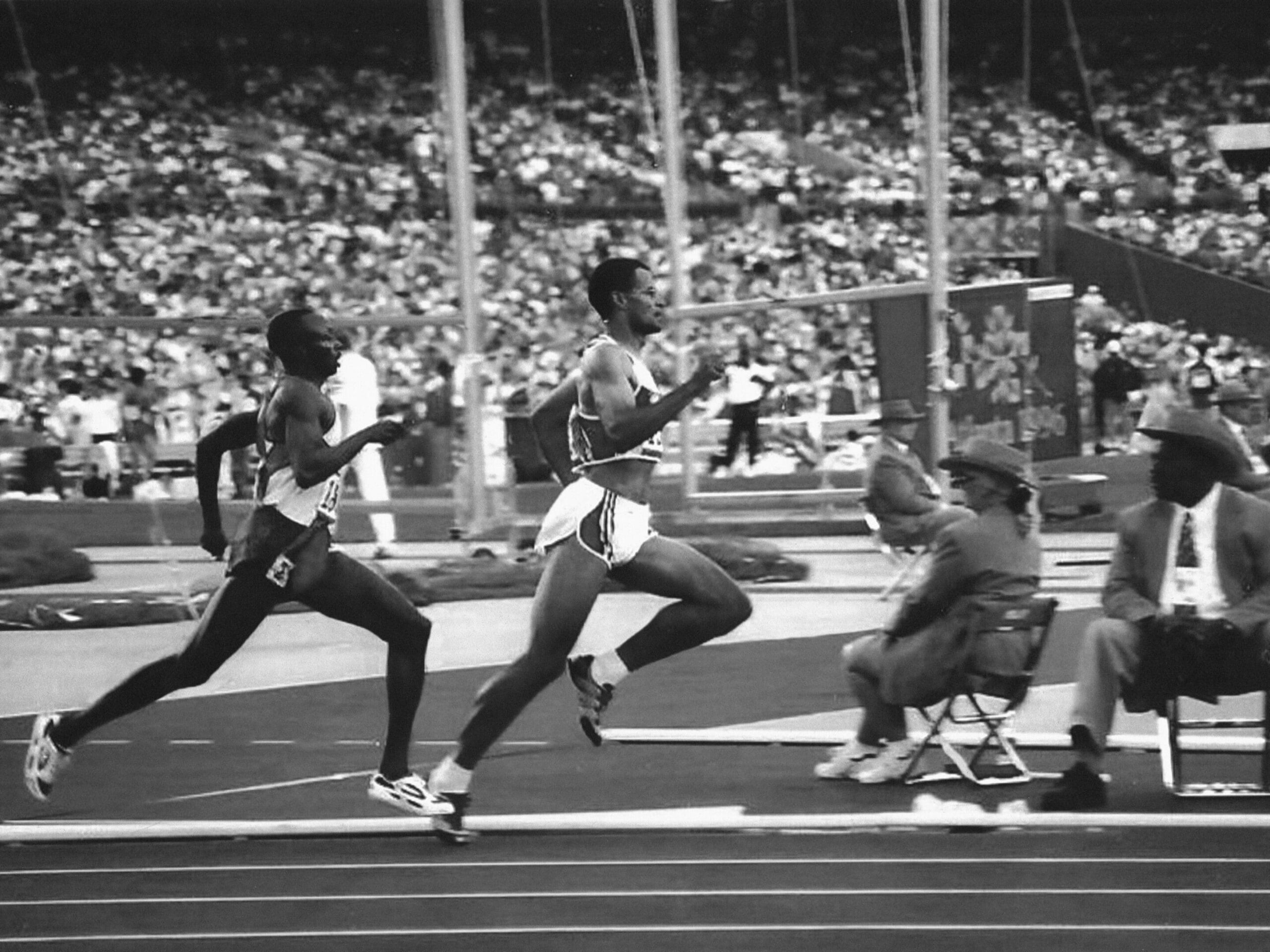 During a Type I Meeting Room event, two athletes sprint on a track amidst the roar of the crowd in the stadium.