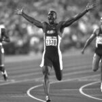 Athlete in USA uniform, captured by PCN Photography, jubilantly crosses the finish line with arms outstretched during a track event.