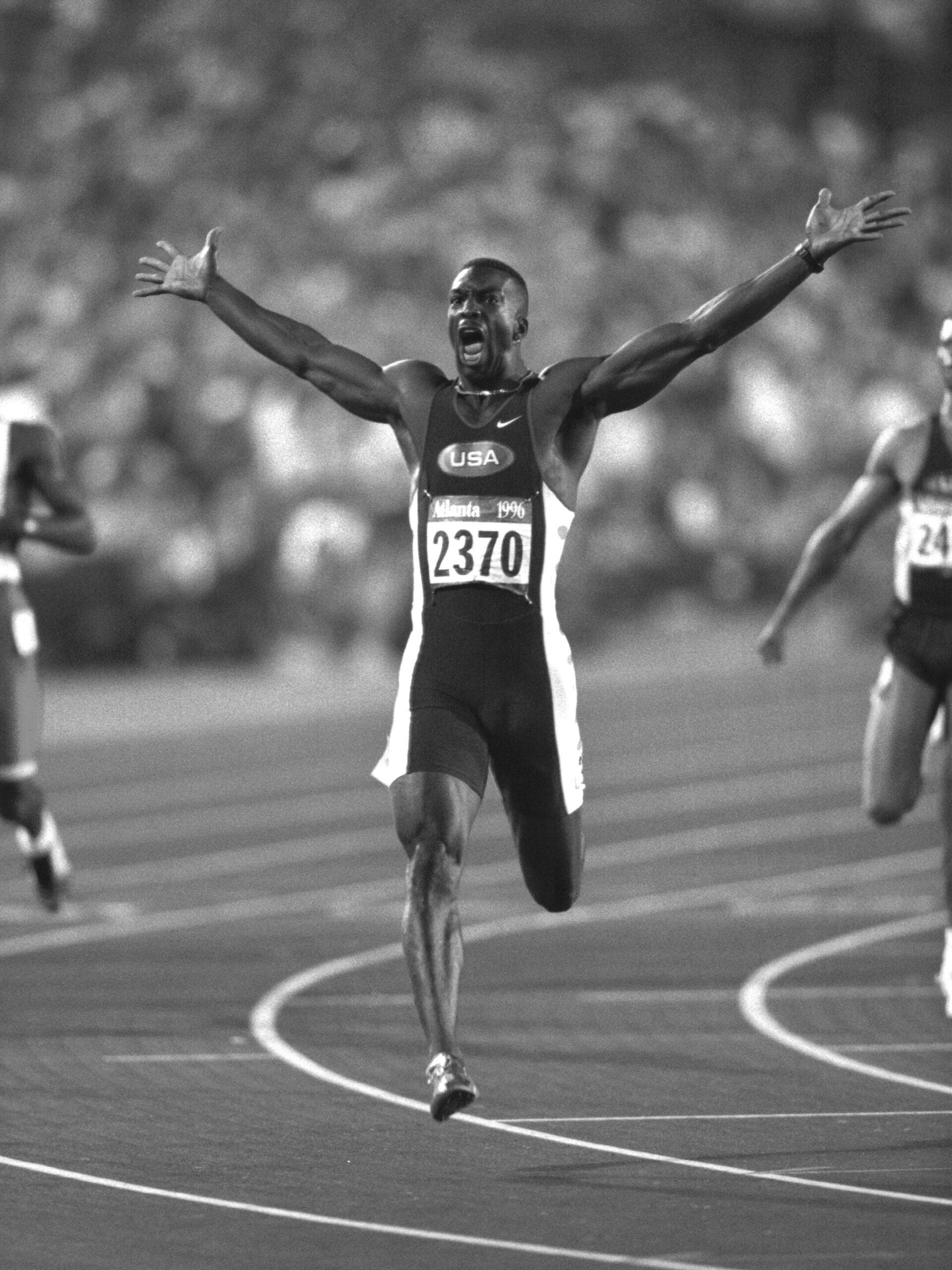 Athlete in USA uniform, captured by PCN Photography, jubilantly crosses the finish line with arms outstretched during a track event.