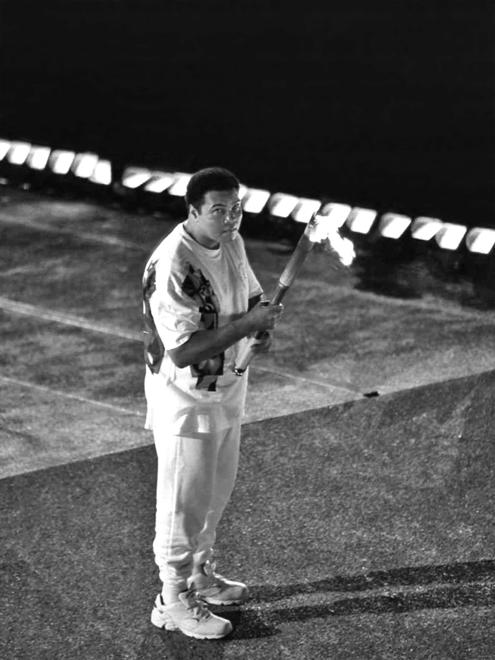 A person in sports attire, embodying the spirit of Sportfolio, holds a lit torch while standing on a sectioned pavement at night.