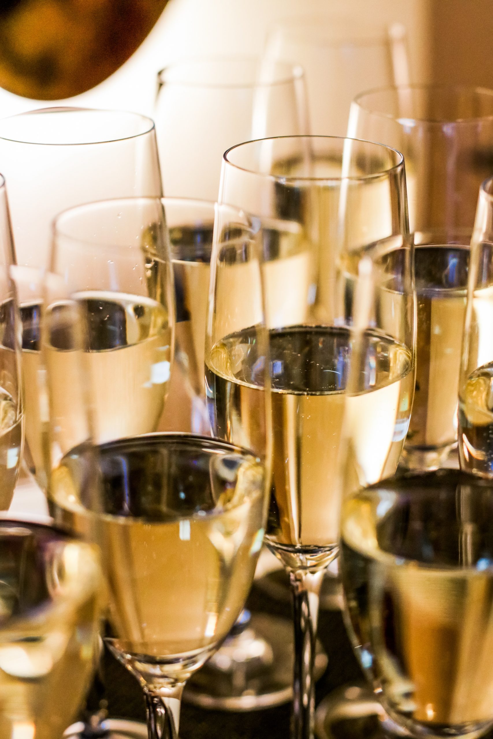 Several champagne glasses filled with bubbly liquid closely arranged under warm lighting.