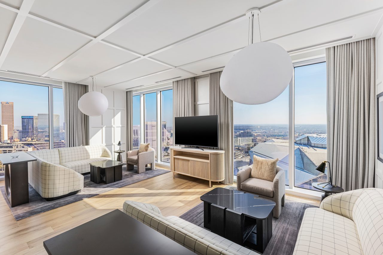 Experience a presidential ambiance in this modern living room with a city view, featuring light-colored sofas, a large TV on a wooden stand, circular ceiling lights, and floor-to-ceiling windows that invite an abundance of natural light.