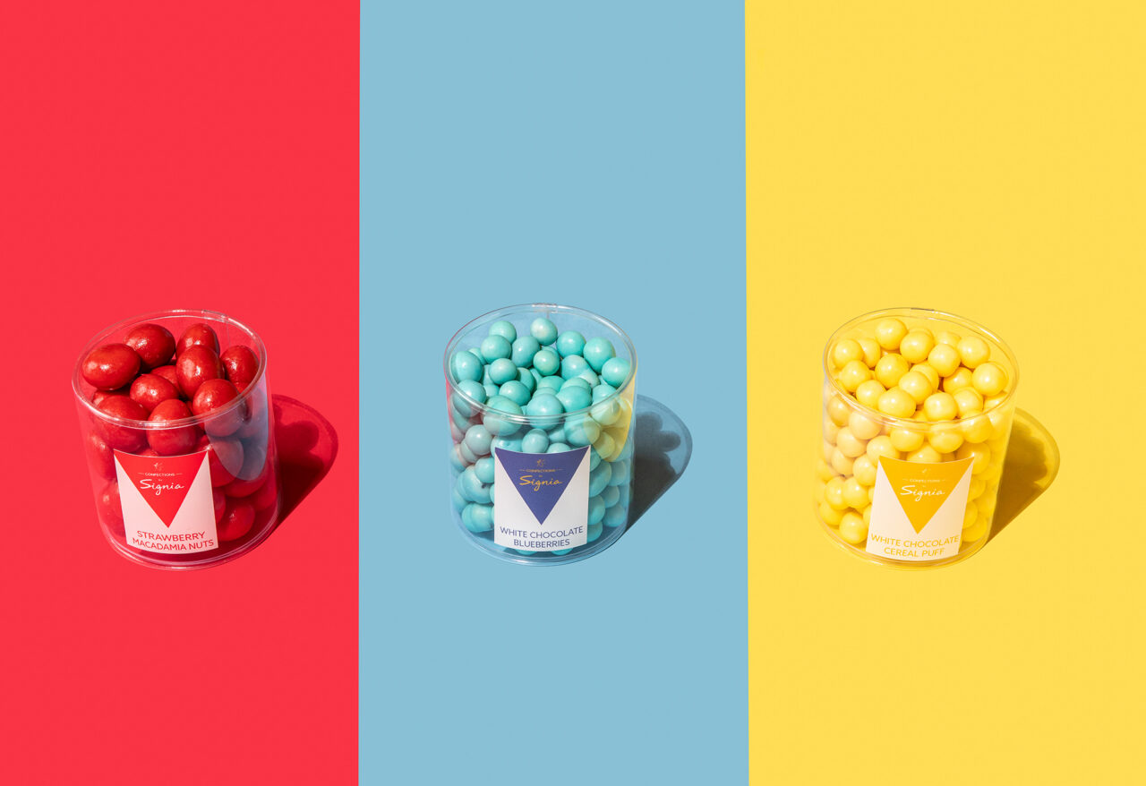 Three clear containers of candy—red, blue, and yellow—sit side by side on matching colored backgrounds: red, blue, and yellow, creating a playful display reminiscent of the fun you’d find at Friendship Market.