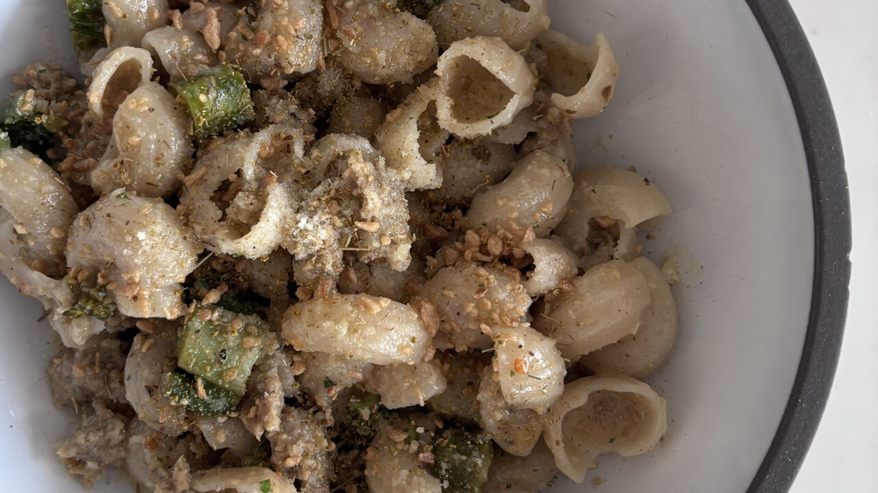 A white bowl filled with orecchiette pasta, chopped green vegetables, ground meat, and a sprinkling of grated cheese and seasonings.