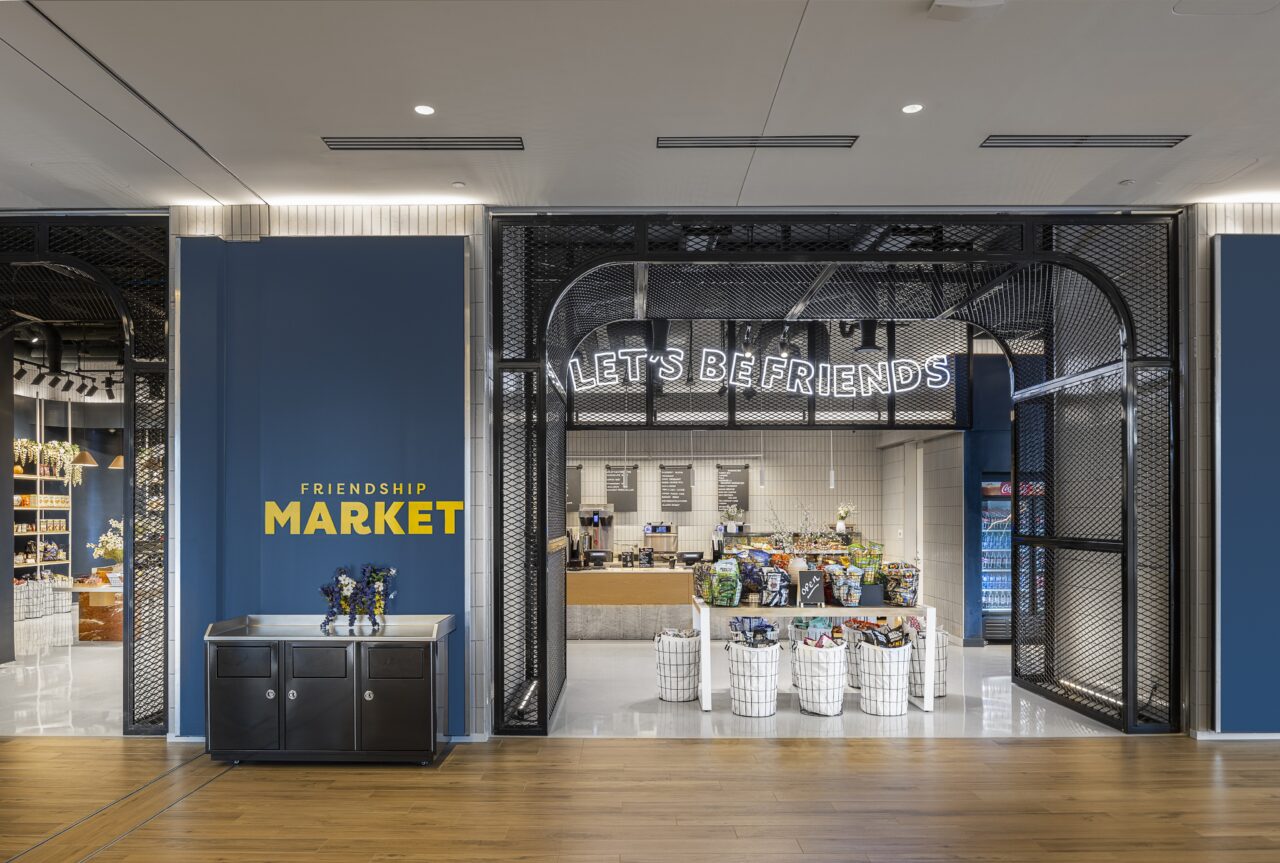 Entrance to the "Friendship Market," where large, open metal arches welcome you. Various products are displayed enticingly, and a sign above warmly invites with the words, "Let's Be Friends.