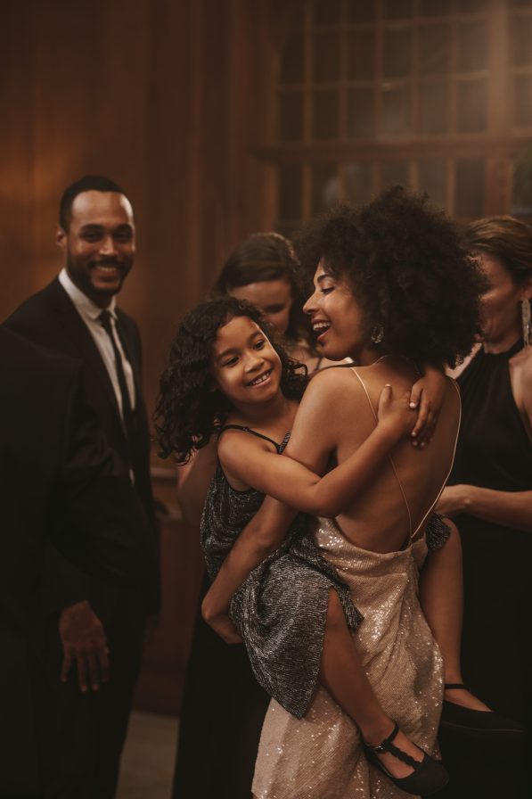 Group of smiling adults in formal attire, one woman holding a laughing child.