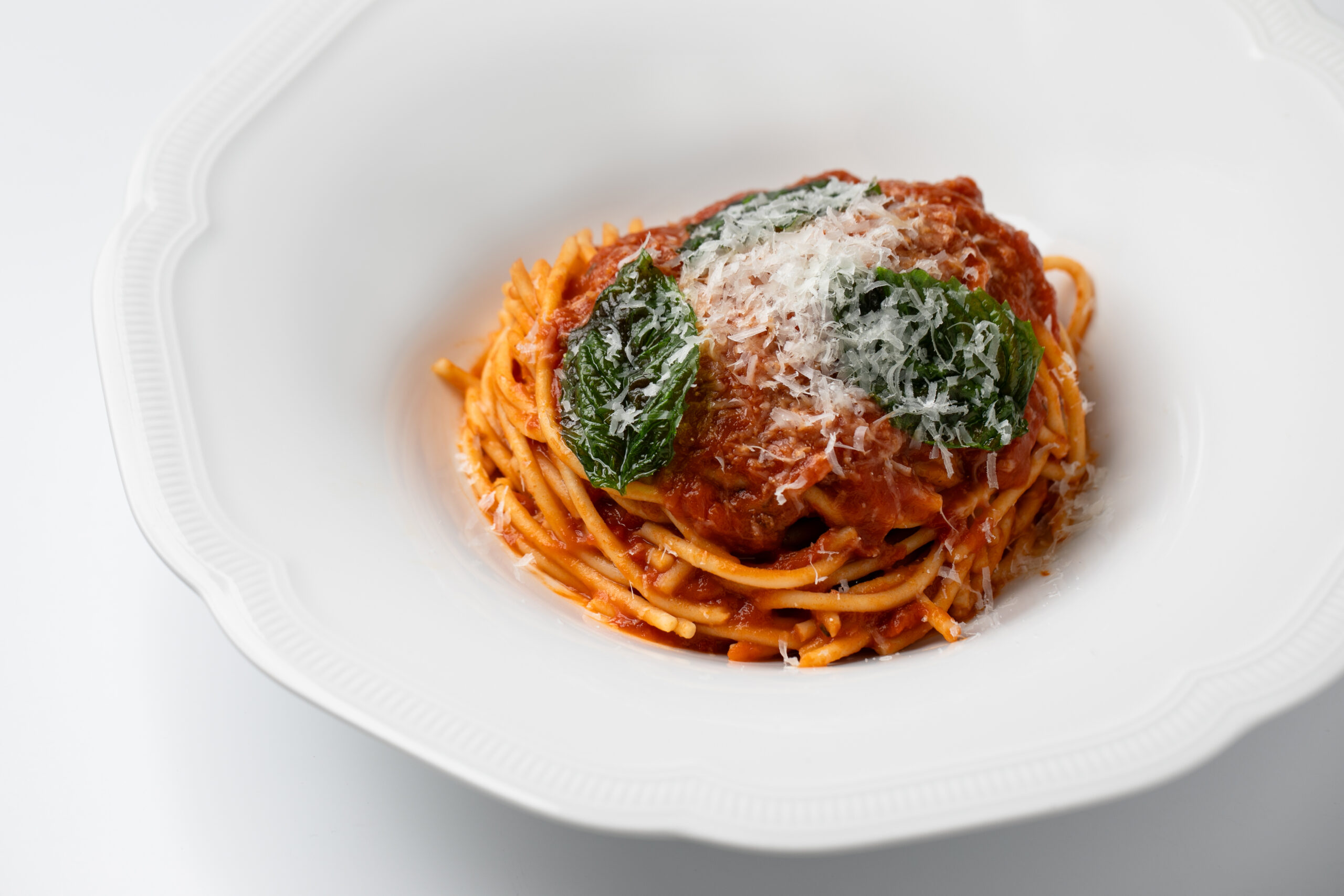 Plate of spaghetti with tomato sauce, garnished with grated cheese and basil leaves, served on a white dish.