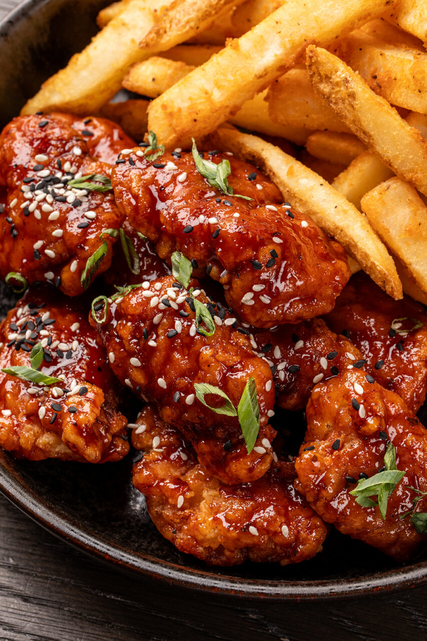 Plate of crispy French fries and glazed chicken wings topped with sesame seeds and chopped green onions.
