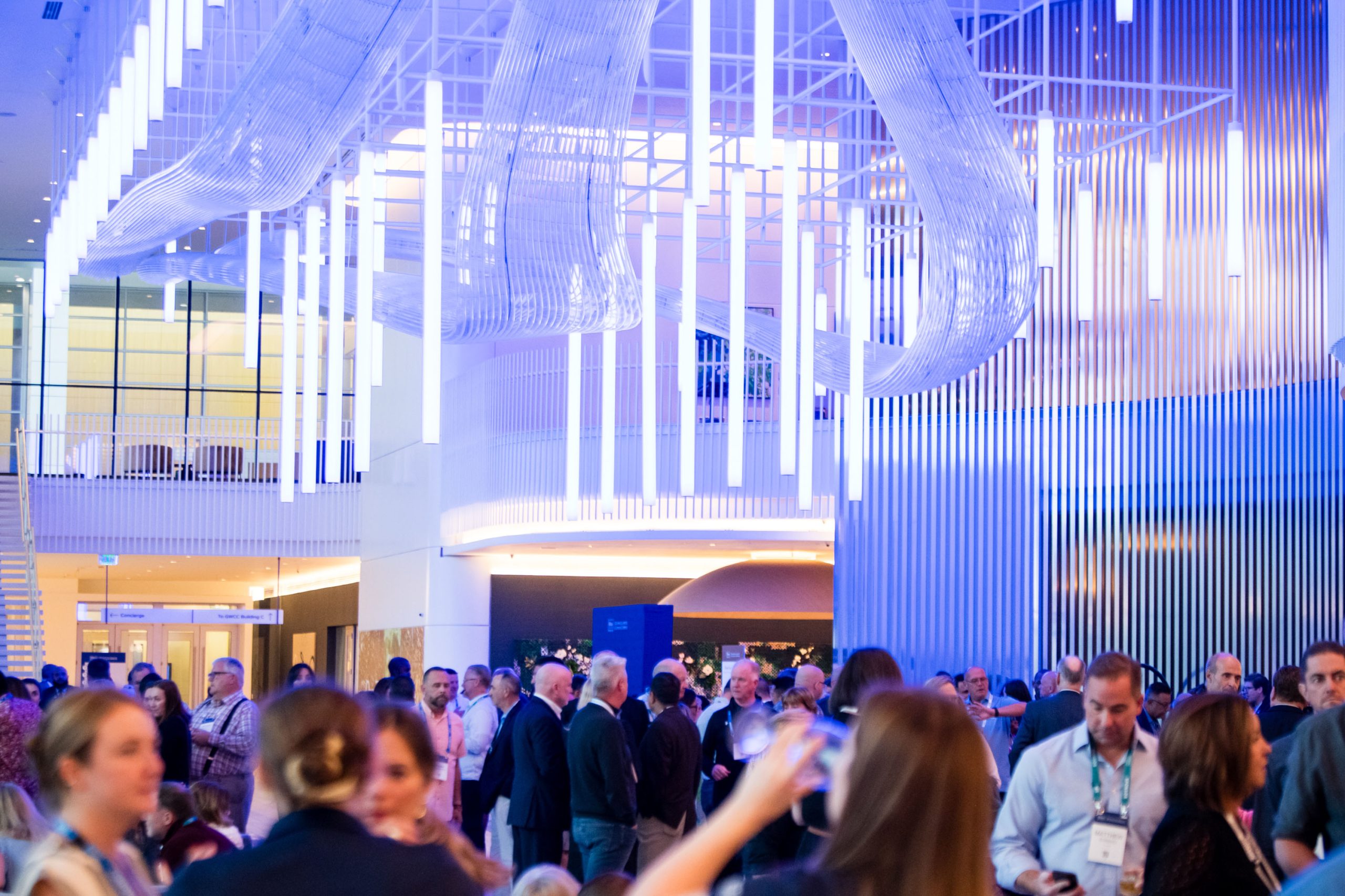 People attending a networking event in a modern venue with blue lighting and a large, artistic ceiling installation.