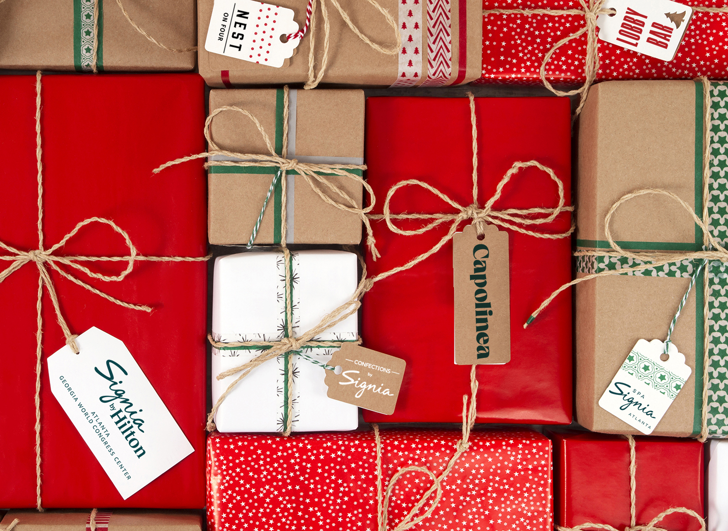 Assorted gift boxes wrapped in red and brown paper with twine, some featuring holiday tags and festive patterns, arranged closely together.