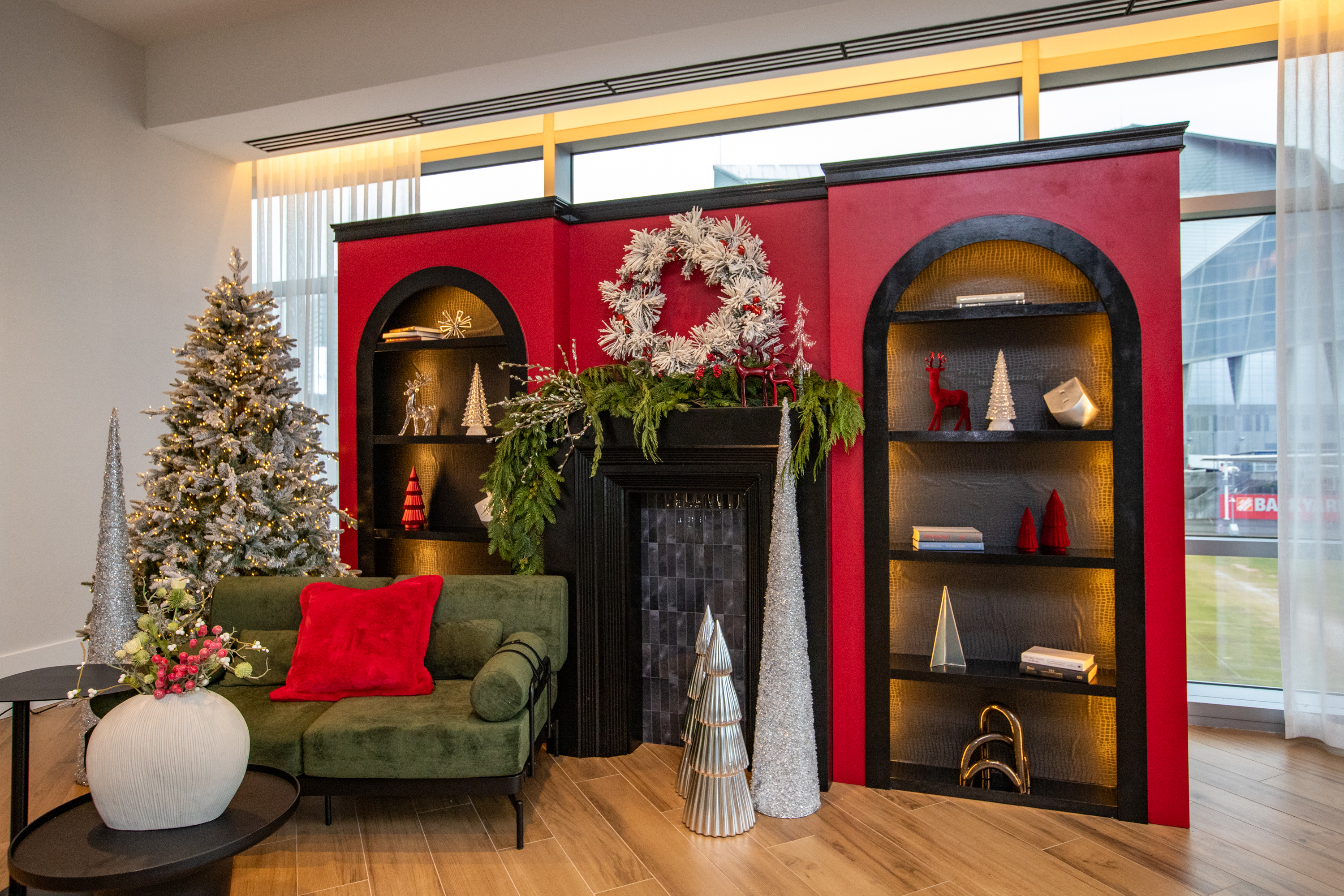 A decorated living room with a green couch, a Christmas tree, and shelves with holiday ornaments, wreaths, and greenery surrounding a fireplace.