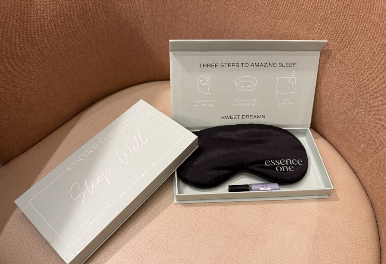 A sleep kit on a chair includes a premium sleep mask in black, a small tube, and packaging with sleep instructions and “essence one” branding.