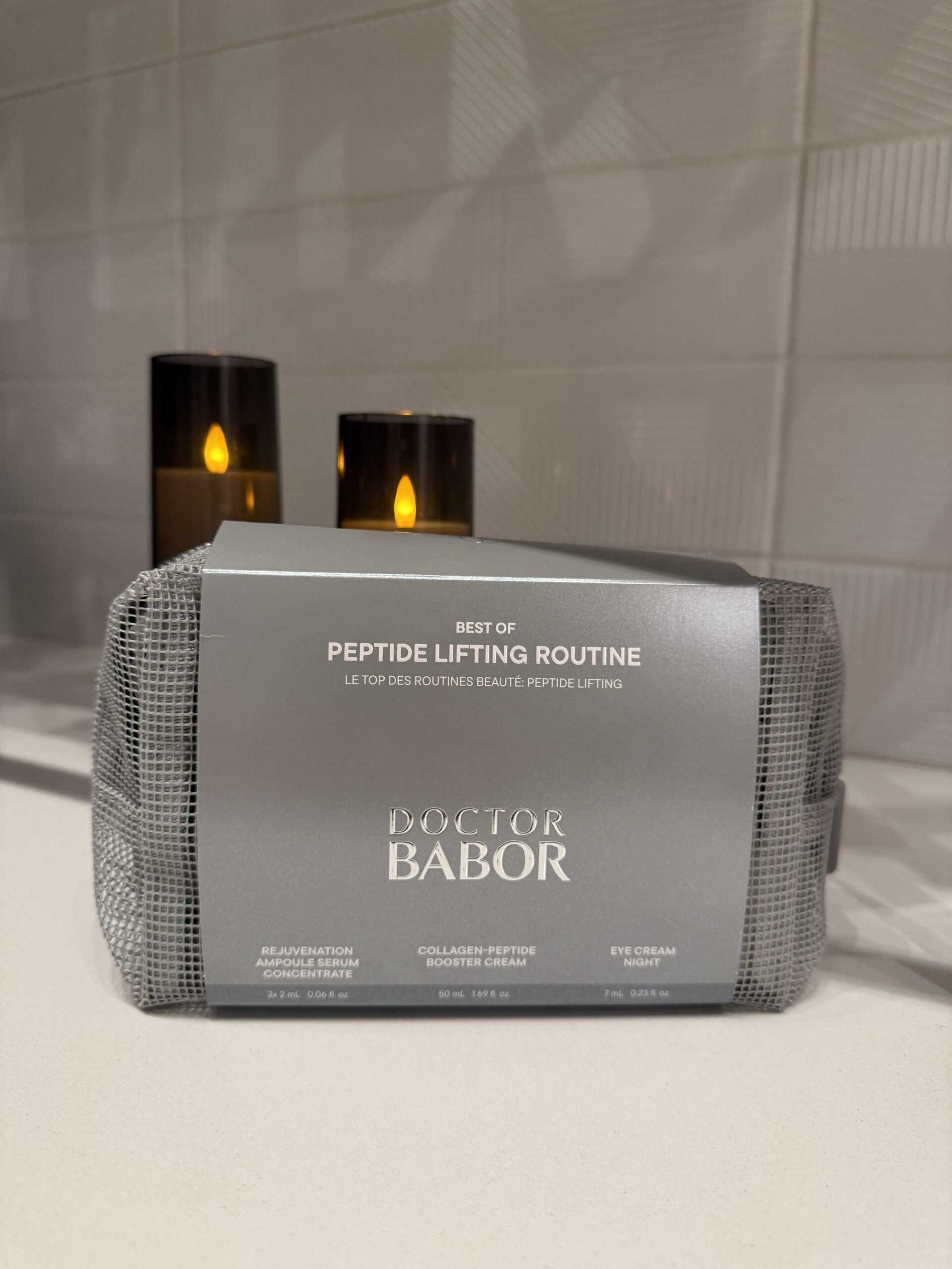A Doctor Babor Peptide Lifting Routine skincare set is displayed on a counter with two lit candles in the background.