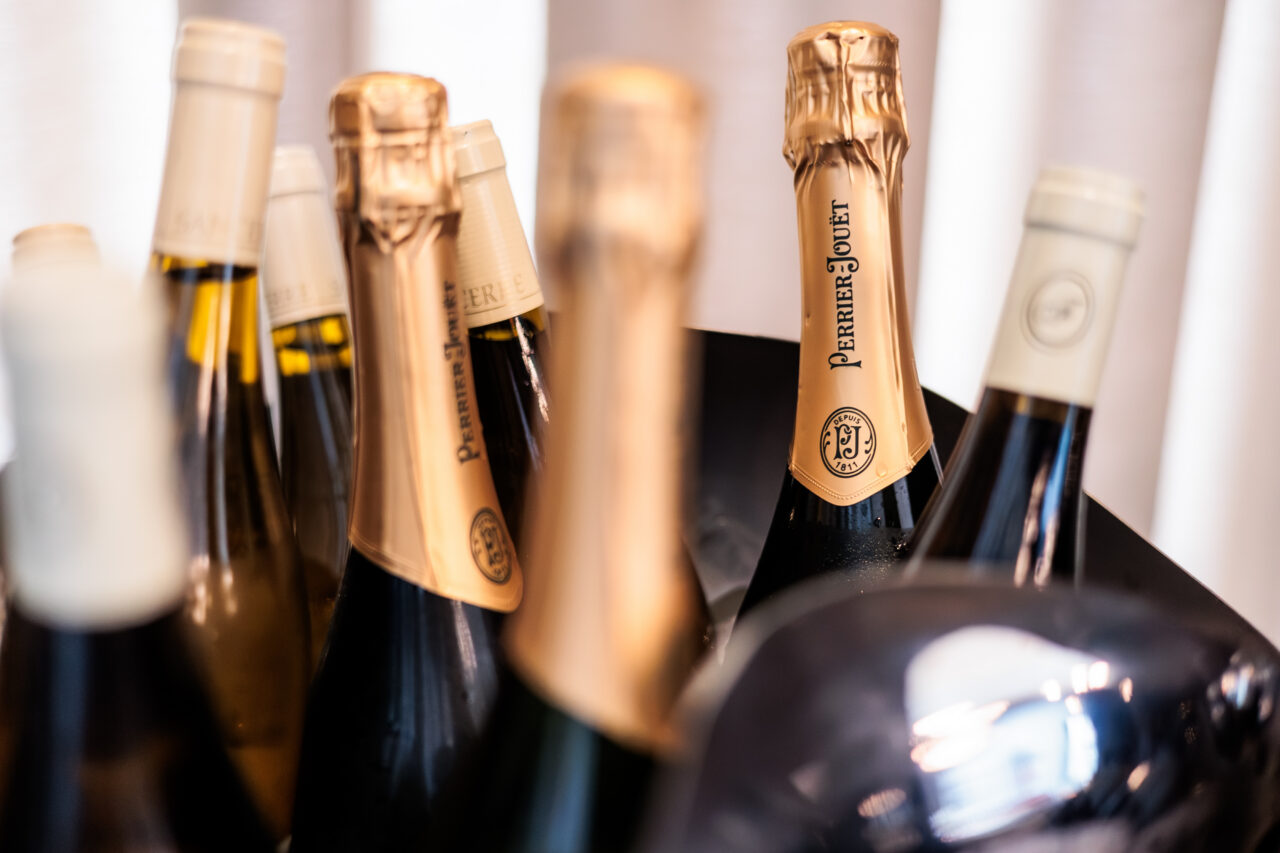 Several bottles of champagne, including one labeled Perrier-Jouët, are displayed together in a bucket or cooler, with gold and cream foil tops visible.
