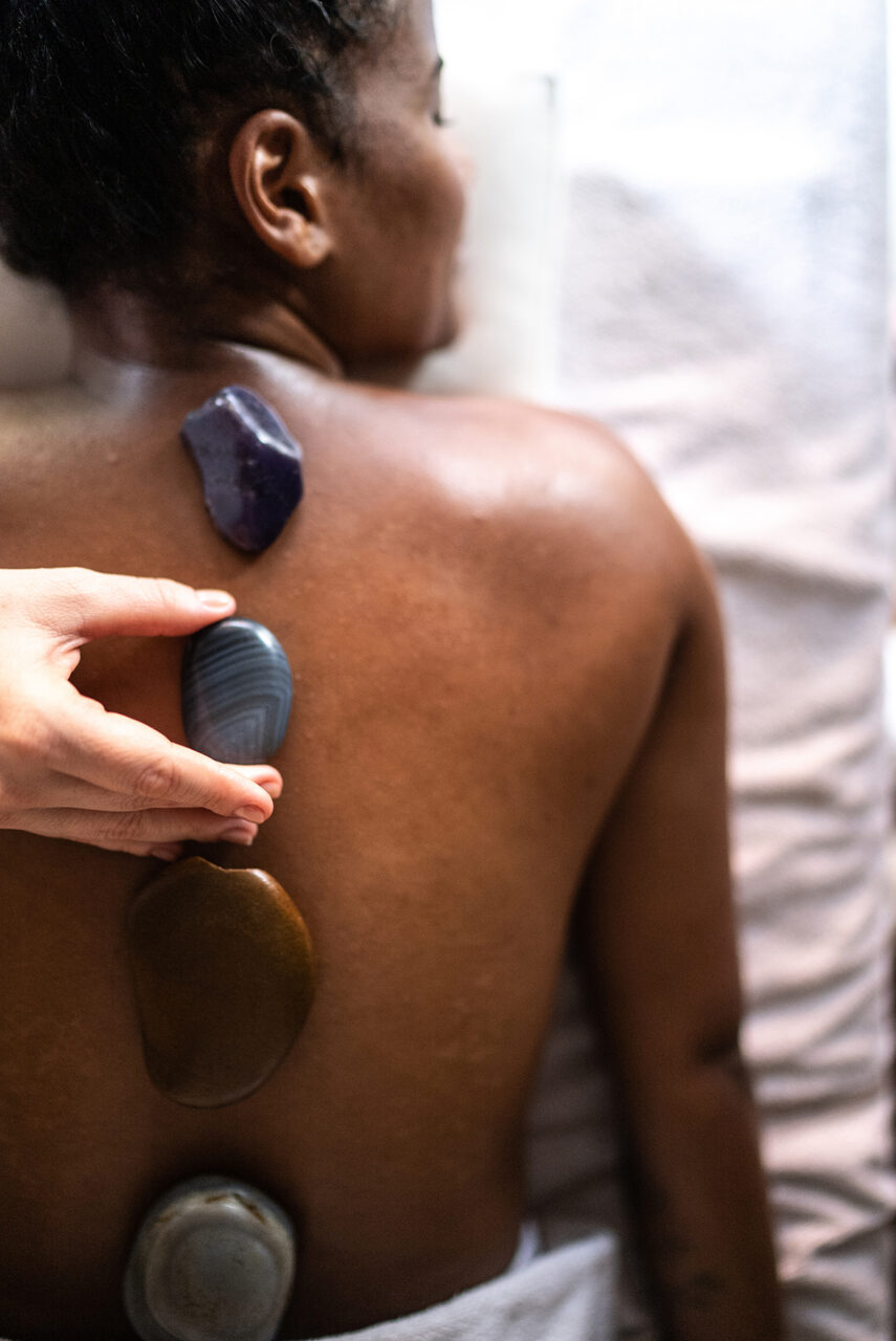 A person lies face down with four polished stones placed along their back as part of a stone therapy treatment.