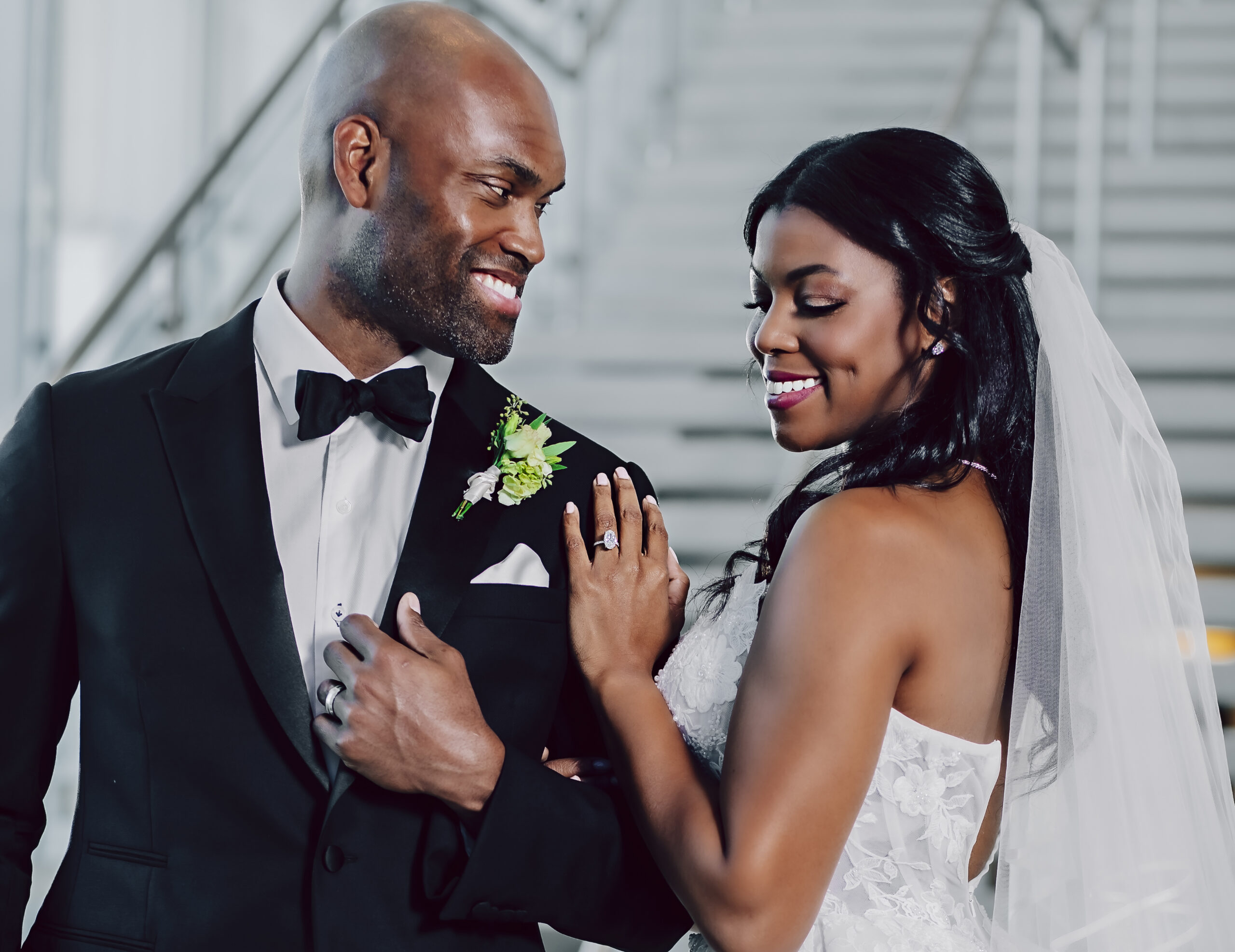 A bride and groom in wedding attire look lovingly at each other.
